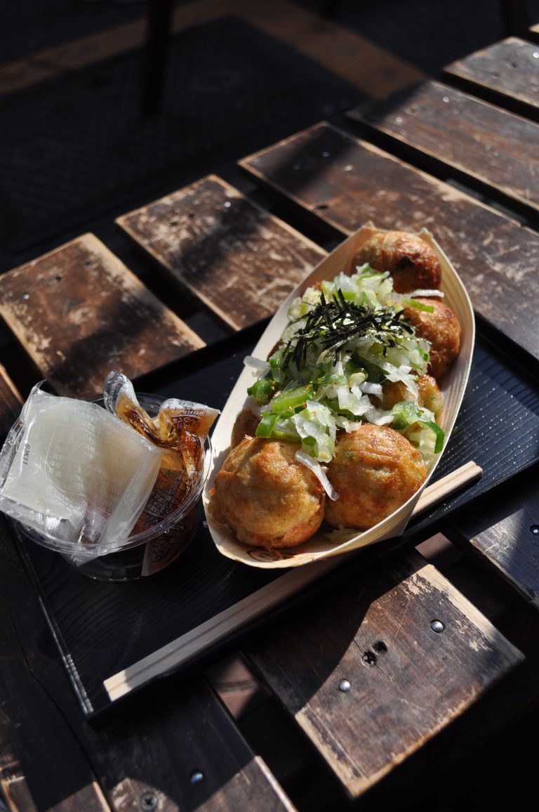 Takeaway takoyaki and sauces on a wooden bench with shadows, Tokyo, Japan.