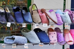 Various styles of slippers and casual shoes displayed on a metal rack in a street market with price tags in euros.
