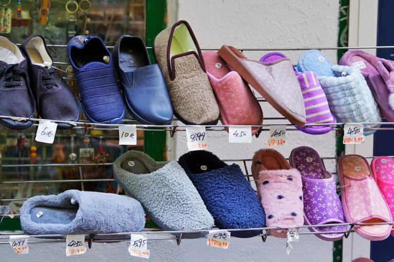 Various styles of slippers and casual shoes displayed on a metal rack in a street market with price tags in euros.