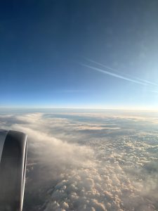 Image taken from the window of an airplane. The engine is to the left and clouds across the horizon in the main image
