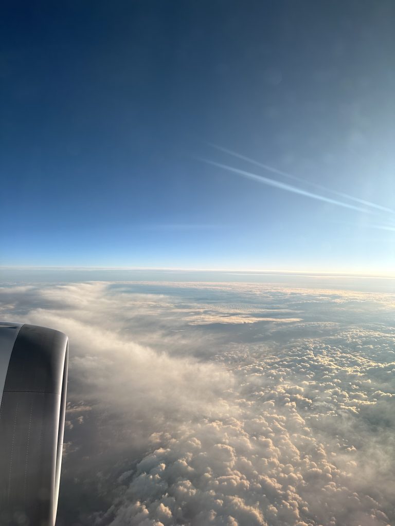 Image taken from the window of an airplane. The engine is to the left and clouds across the horizon in the main image