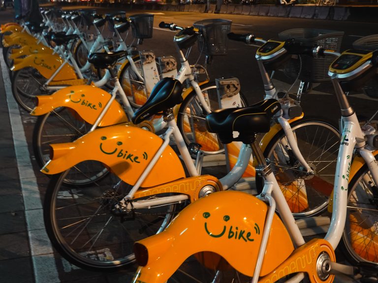 A row of orange and white bicycles with smiley faces and the word “bike” on their rear fenders, docked at a bike-sharing station at night in Taipei.