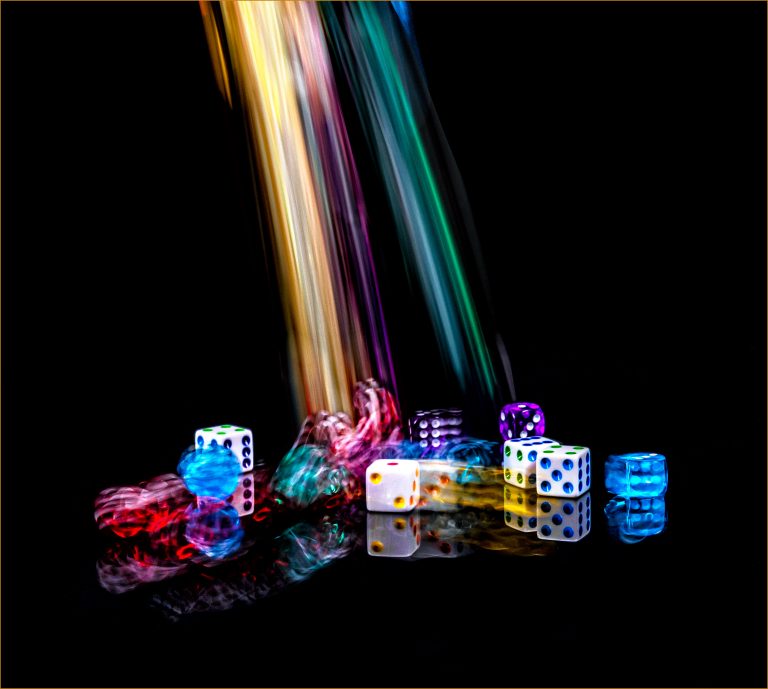 A Waterfall of dice. A dozen (or more) of colorful dice dropped on a black reflective surface. Long exposure.