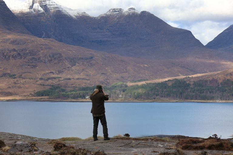 Man taking photos on the edge of Loch Torridon, flanked by the Torridon Mountains, Scottish Highlands