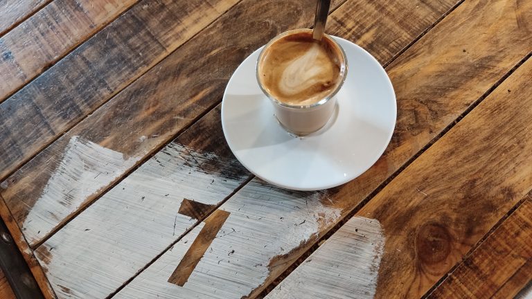 Wooden tabletop latte mug in a white ceramic mug with a table number. Number 7 on the table. Treated wood table.