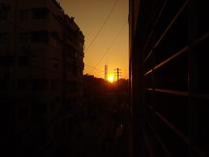 A sunset view between two buildings with silhouette of power lines and a building under construction in the background.