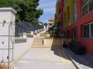 Stone steps go up between the metal fence of the park and the hotel wall