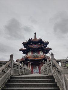 View larger photo: The image is of a cloudy sky and a building with stairs leading up to it in Taipei. It features Chinese and Japanese architecture elements, bright colours (red, white, etc.)