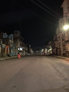 View larger photo: A nighttime view of people walking on a street, with buildings and utility poles against a dark sky.