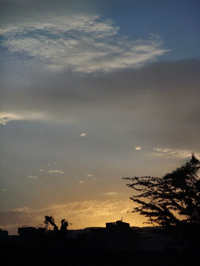 Silhouette of a cityscape against a twilight sky with scattered clouds.