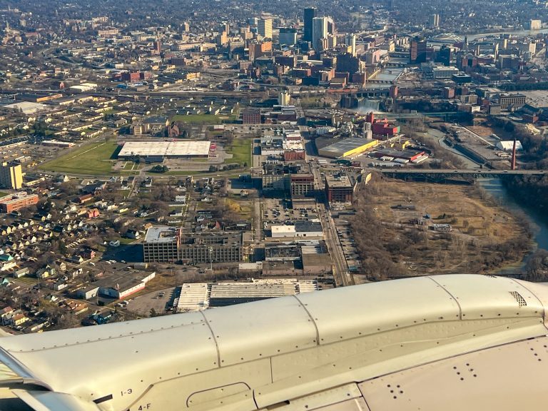 A view of downtown Rochester, New York, over the wing of an airplane. The Genesee River runs through it with High Falls in the photo.