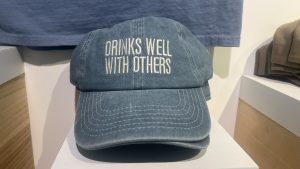Blue canvas baseball hat with the text “Drinks Well With Others”
