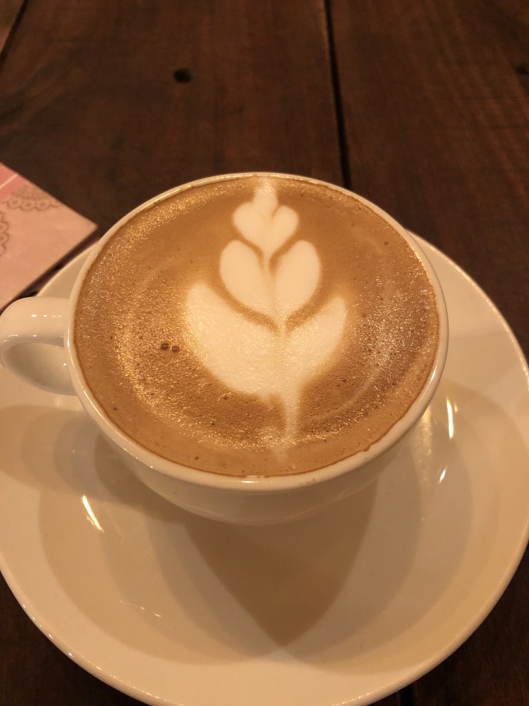 A cup of cappuccino with latte art on top, on a saucer, placed on a wooden table.