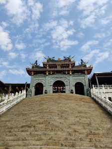 The photo is of a temple in Taipei. It is a historic site and possibly a temple or shrine. The architecture is made of stone, temple is set at the center of the photograph, around you can see some clouds in the sky.