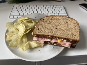 Ham sandwich on a plate with chips in front of a keyboard.
