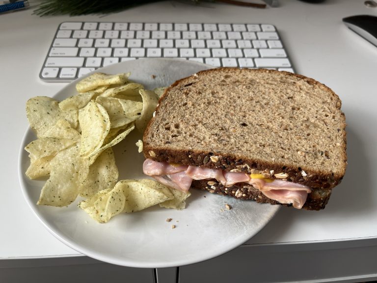 Ham sandwich on a plate with chips in front of a keyboard.