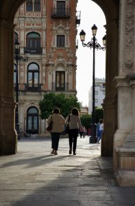 View larger photo: Two women chatting whilst walking through a stone arch in the center of Seville.