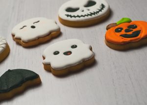 A selection of Halloween-themed decorated cookies in the shapes of ghosts and pumpkin on a light wooden surface.
