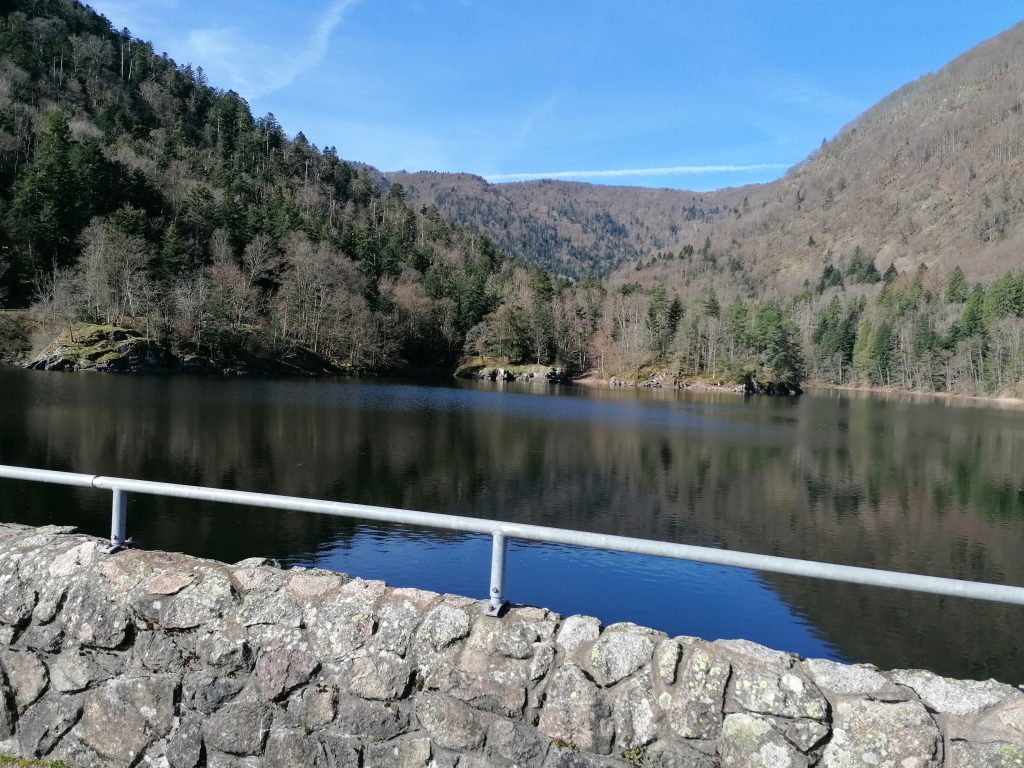 Lac d’Alfeld dam, south of the Vosges mountains in Alsace. Stone bridge over a lake surrounded by mountains.