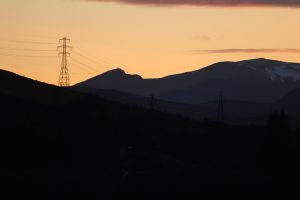 Electricity pylon in silhouette on a hill against a mountainous sunset sky, Scottish Highlands