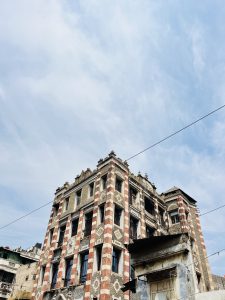 An old ornate building with distinctive red and white striped patterns on its facade, set against a cloudy blue sky.