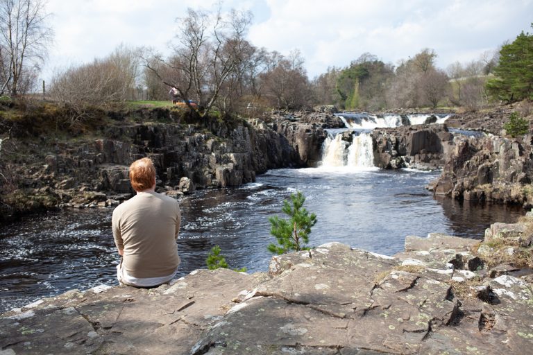 Man sat on the edge of the a cliff with a waterfall in the background