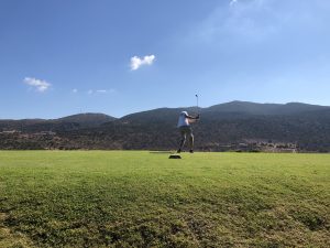 A golfer, taking a swing, a blue sky and hills in the background