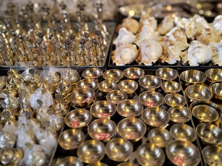 Brass and steel oil lamps displayed alongside conch shells in a shop.