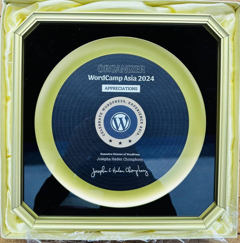 A token of appreciation received by WordCamp Asia 2024 organizers from WordCamp Central. Disc with the WordPress logo and text engraving in a golden frame.