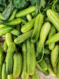 A pile of fresh cucumbers with some green leaves in the background.