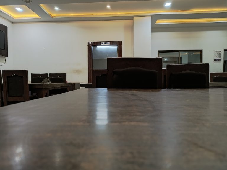 Empty dining area with wooden tables and chairs. The kitchen door is in the background.