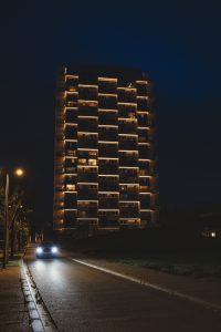 Car driving by a highrise apartment, at night.