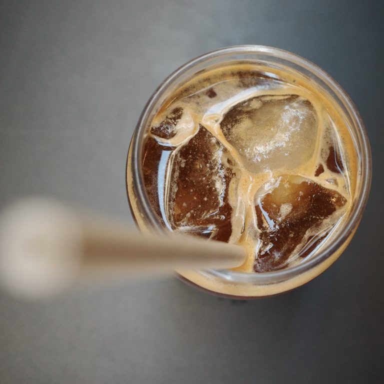 Grass of iced coffee with drinking straw on a gray background