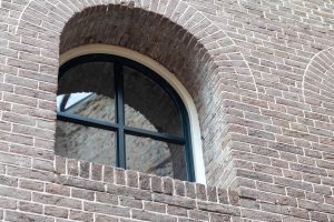 Arched window with black metal frame set in a brick wall, viewed from an angle at Fort Pannerden, the Netherlands
