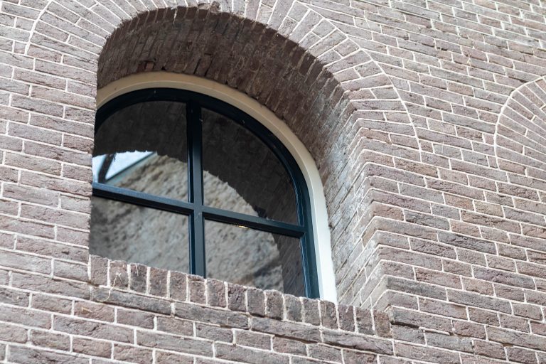 Arched window with black metal frame set in a brick wall, viewed from an angle at Fort Pannerden, the Netherlands