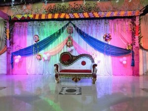 A beautifully decorated stage with colorful draperies, floral arrangements, and balloons sets the scene for a festive event. A regal-looking sofa in the center adds an elegant touch to the overall decor.