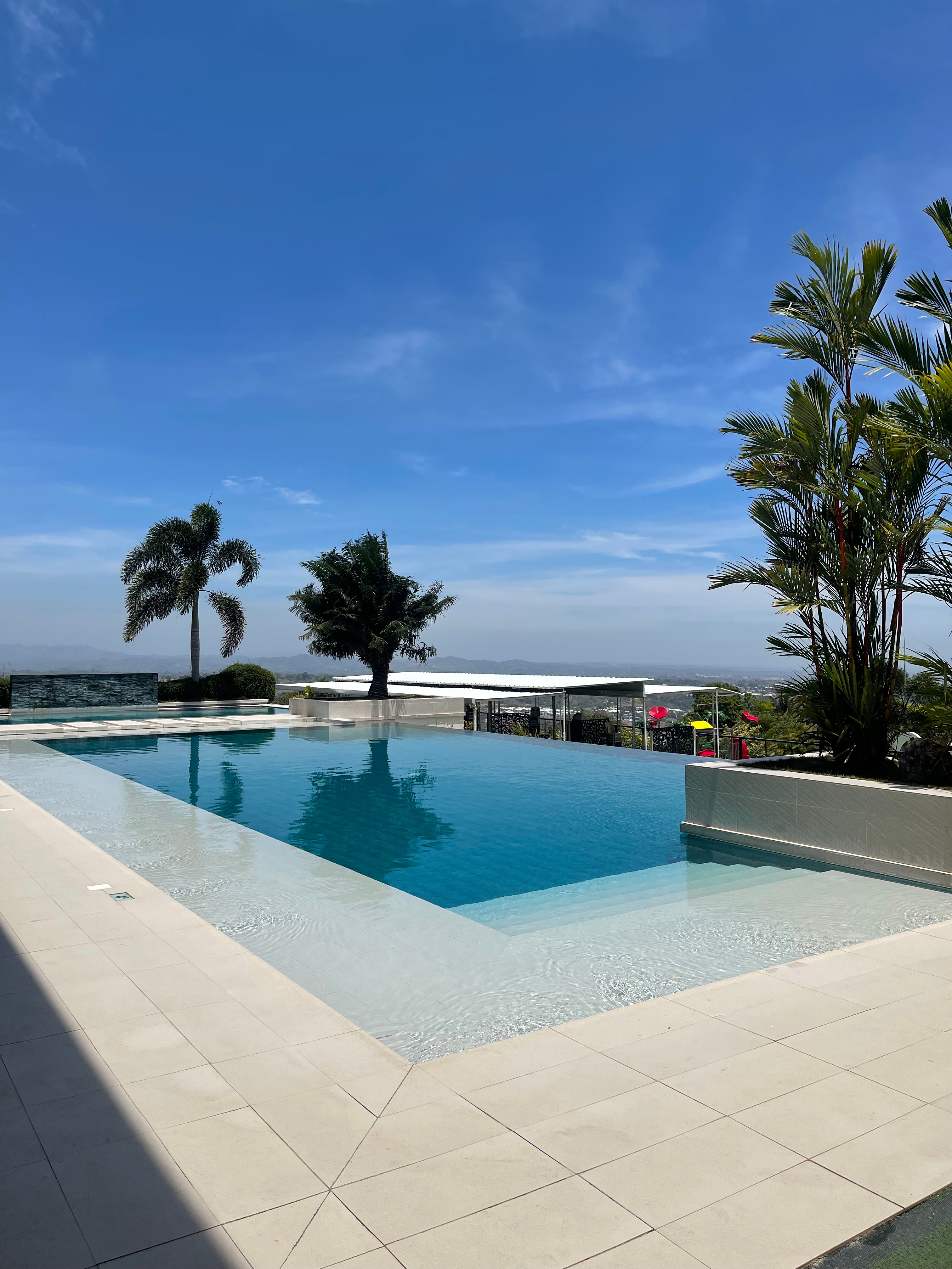 In ground swimming pool with steps down into it, palm trees, a bright blue sky and mountains in the distance