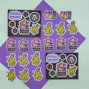 An assortment of colorful stickers and a framed collection related to WordPress, including images of the WordPress logo mascot, Wapuu, displayed on a dual-tone geometric background.