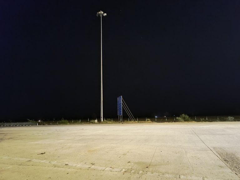 A deserted toll tax area at night with a solitary lamppost and a starry sky overhead.