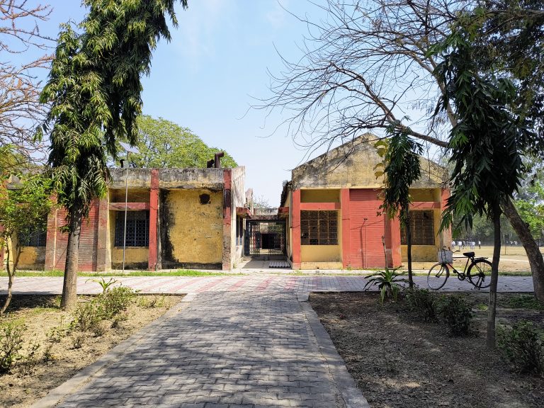 A deserted collegeyard with a bicycle parked beside a weathered building, surrounded by trees under a clear sky.