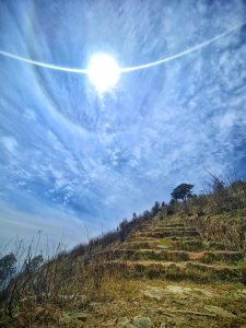 Scenic view of a blue sky with fluffy clouds, radiant sun, and a winding trekking path.