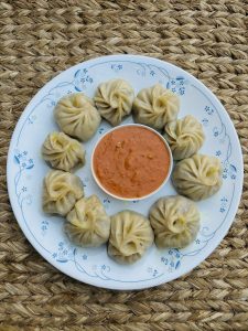 A plate full of chicken momo with pickle in the middle on the top of nepali mat called ‘gundri’ .