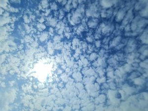 A clear blue sky with fluffy clouds and sunlight streaming through the clouds.