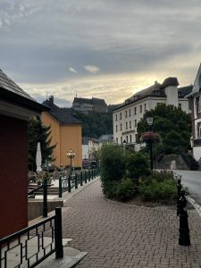 A street in Vianden, Luxembourg, a hill and a castle on top of it and in the background a cloudy sky