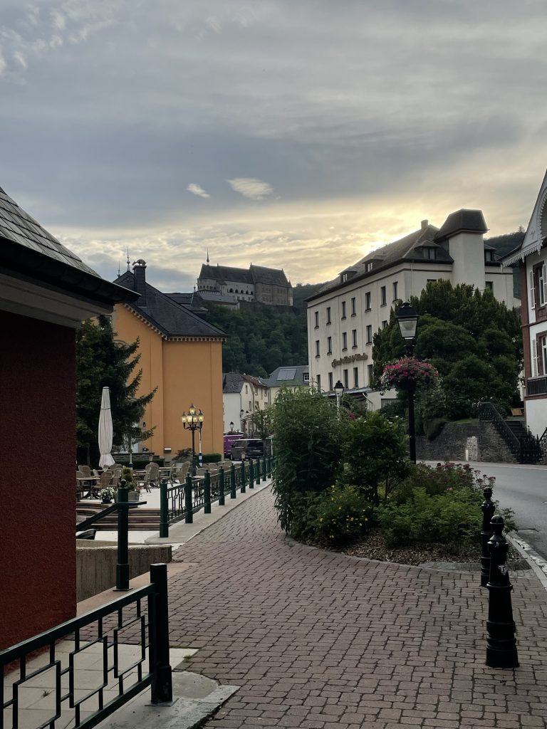 A street in Vianden, Luxembourg, a hill and a castle on top of it and in the background a cloudy sky