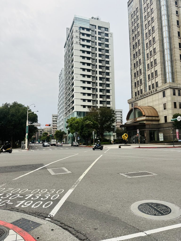 A tall building, clean road and some vehicles passing in Taipei, Taiwan.