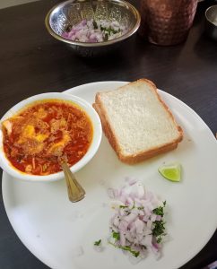 Spicy kolhapuri misal served on table with onion, lemon & bread.