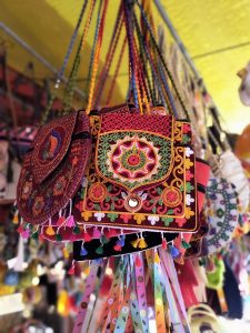 Colorful embroidered sling bags with vibrant tassels, displayed at a market stall, showcasing traditional Indian craftsmanship and style.