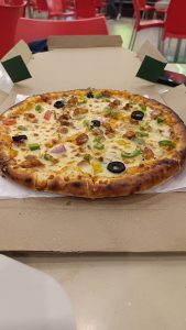 A pizza topped with green and red peppers, onions, black olives, and sausage in a restaurant with red plastic chairs