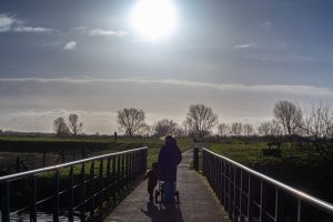 A woman and a child holding hands while walking on a bridge with the sun shining brightly above them.
